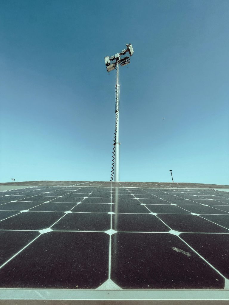 pexels-photo-9799713-9799713 Solar panels under a clear blue sky with a communication tower in the background.